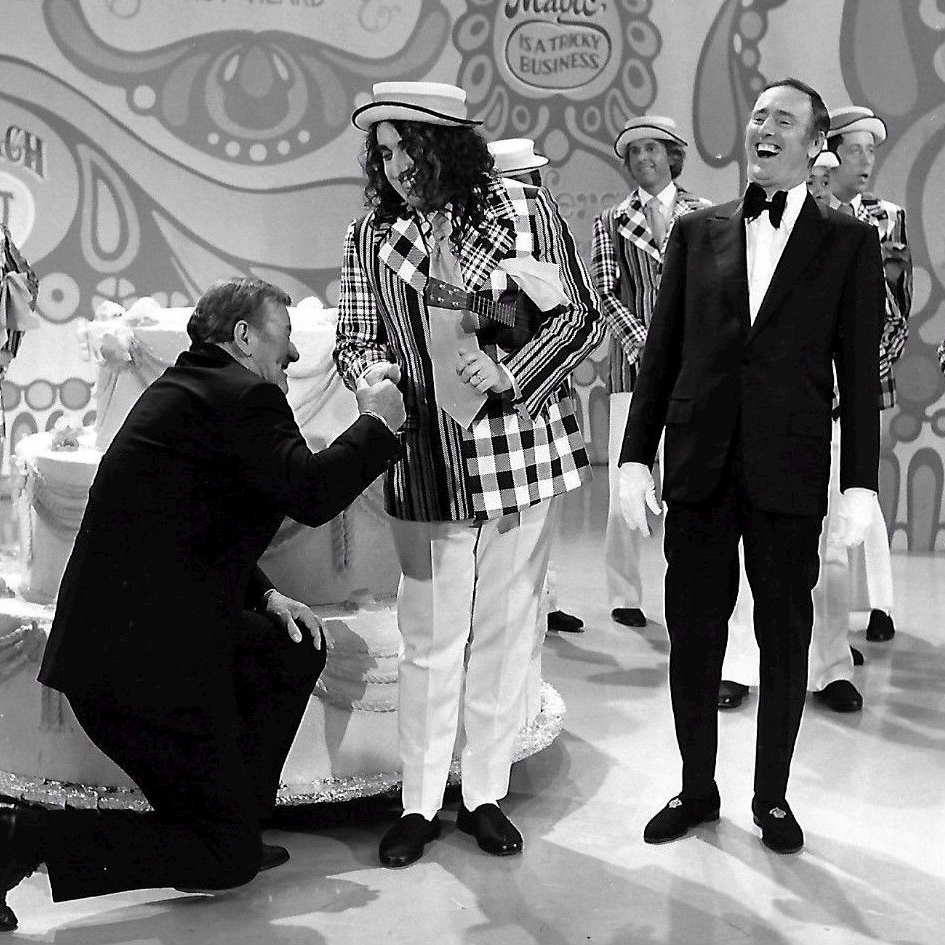 Publicity photo from the 100th episode of the television program Rowan & Martin's Laugh-In. Guest stars are John Wayne and Tiny Tim. Host Dick Martin is pictured, along with past and present cast members from the show.
